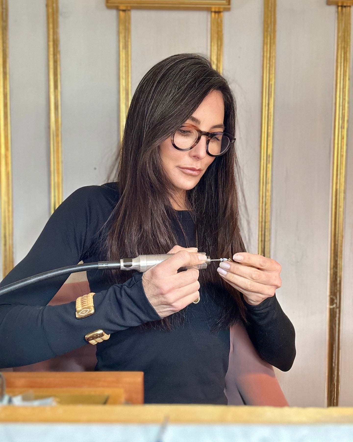 Model wearing cuff and holding drill while making jewelry
