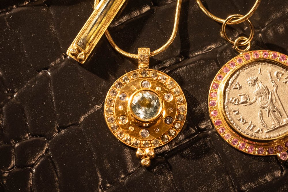 A beautiful mosaic pendant. The Paris & Lily “Dusk” pendant is one-of-a-kind and handcrafted in 22K gold with a 6mm round center aquamarine surrounded by light blue sapphires and diamonds. The pendant has a border of light blue sapphires. Diamonds adorn the chain bail and granules. Shown on a 14K, 16 inch chain.