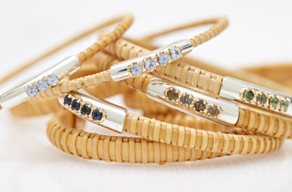 Stack of various colored Sapphire Nantucket Basket Bangles, handwoven from natural cane and rattan, stacked on table