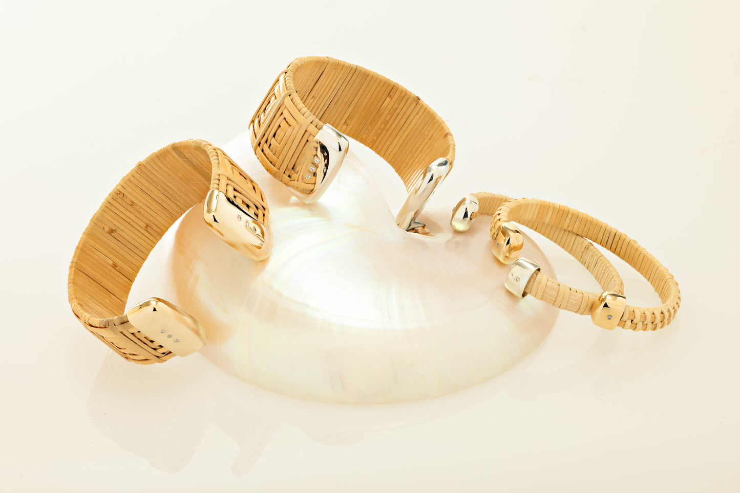 Four Nantucket cuff bracelets gold and silver caps and diamonds sitting atop a seashell