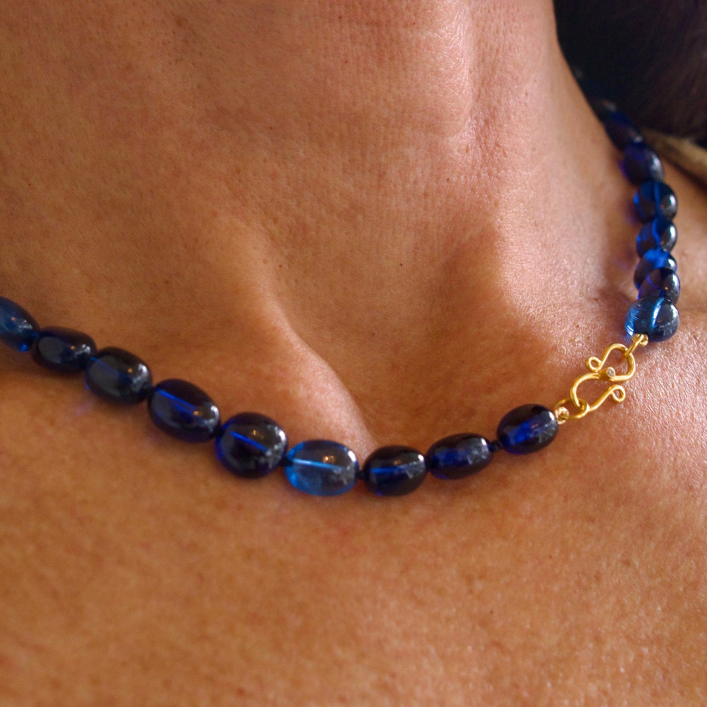 Blue beaded necklace with a gold clasp on a person's neck