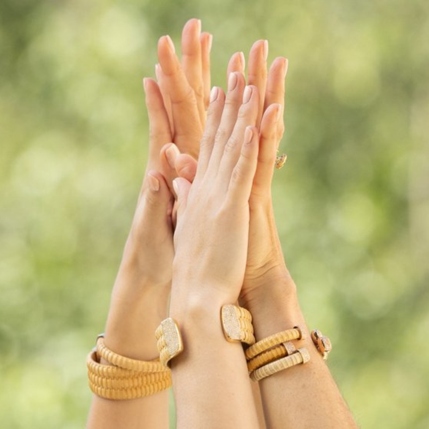 two sets of hands touching with woven bracelets against a blurred nature background