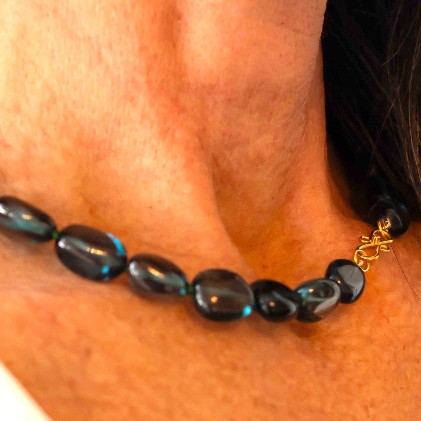 Close up of woman wearing blue beaded necklace with gold clasp around her neck
