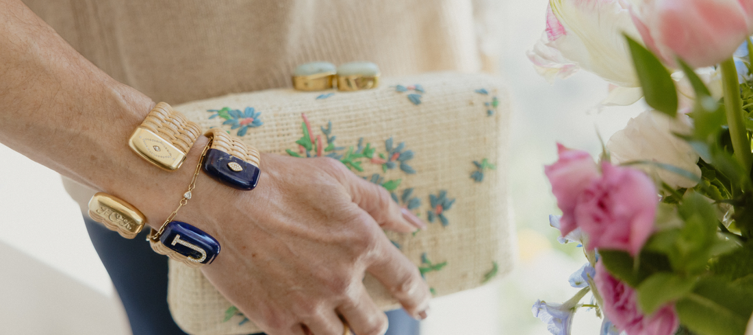 close up of woman holding embroidered woven clutch with floral print and wearing handcrafted woven cuff bracelets with gold and lapis caps on wrist