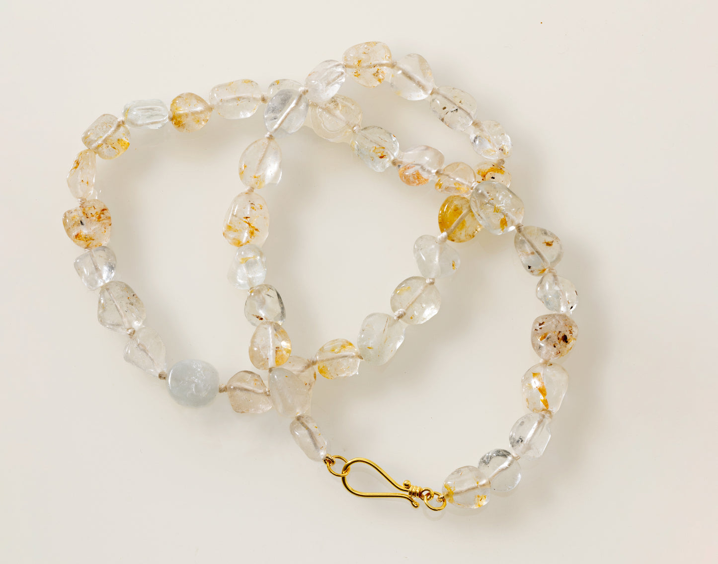 A white topaz pebble necklace with gold silk threading and an 18K yellow gold clasp, laid out on a white surface.