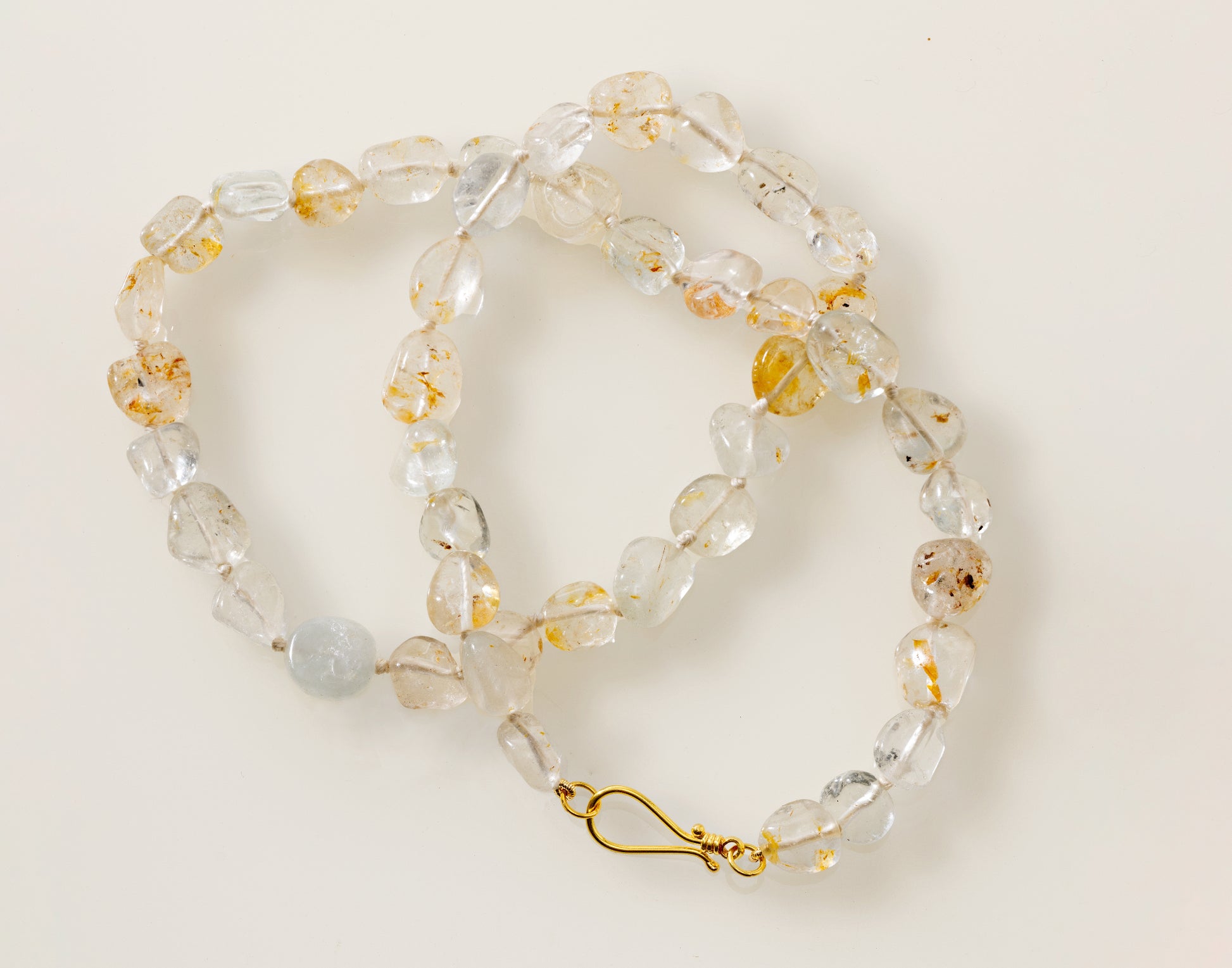 A white topaz pebble necklace with gold silk threading and an 18K yellow gold clasp, laid out on a white surface.