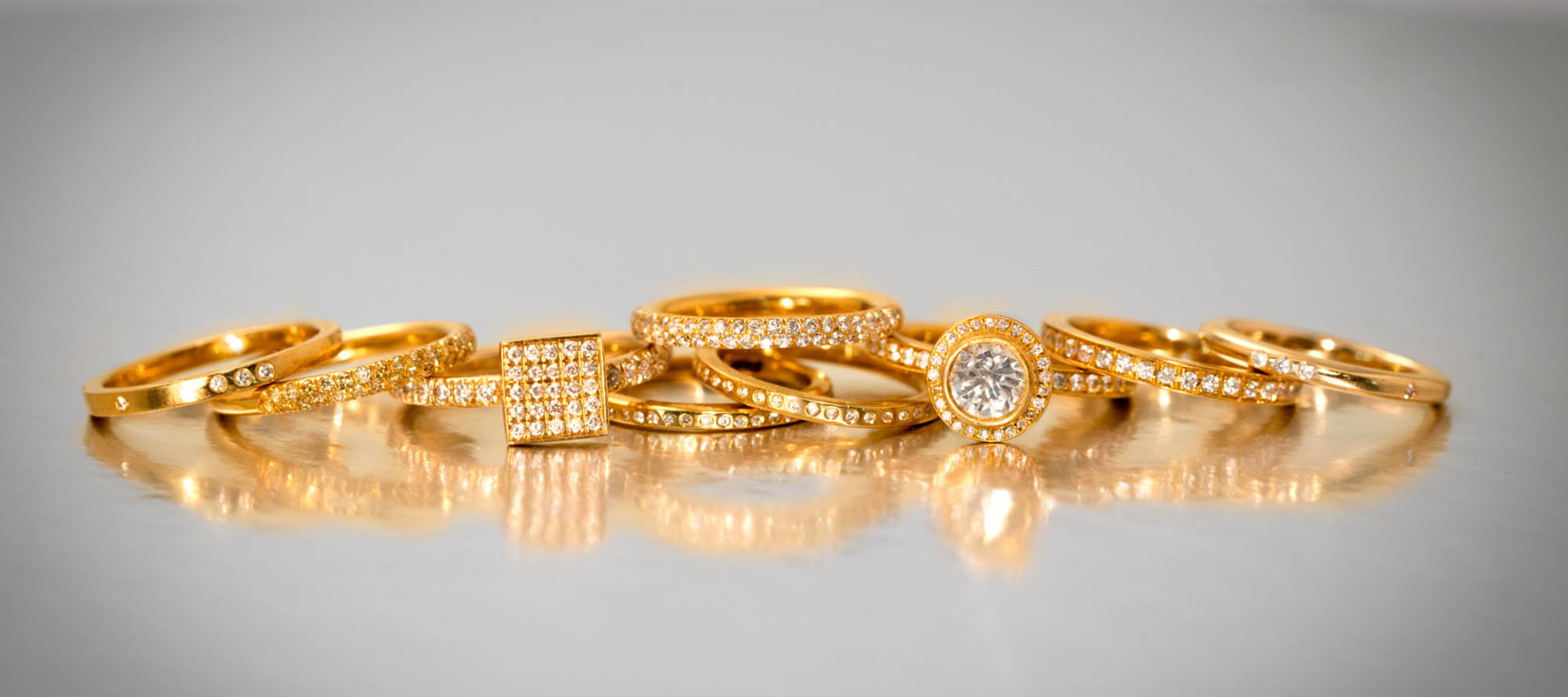 pile of gold and diamond engagement rings on a neutral background