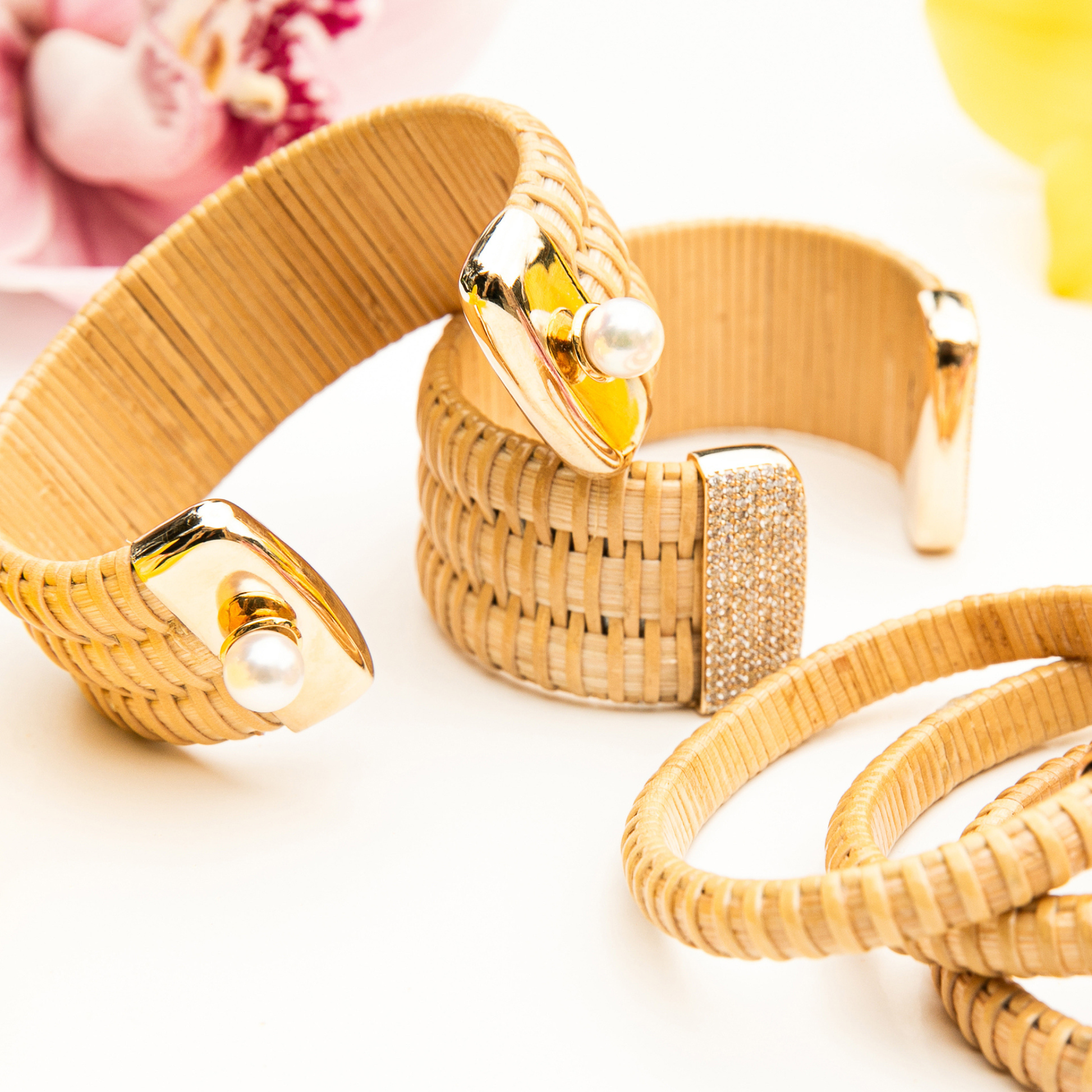 Nantucket basket cuff bracelets on table, some with pearl and some with diamonds, flowers in background