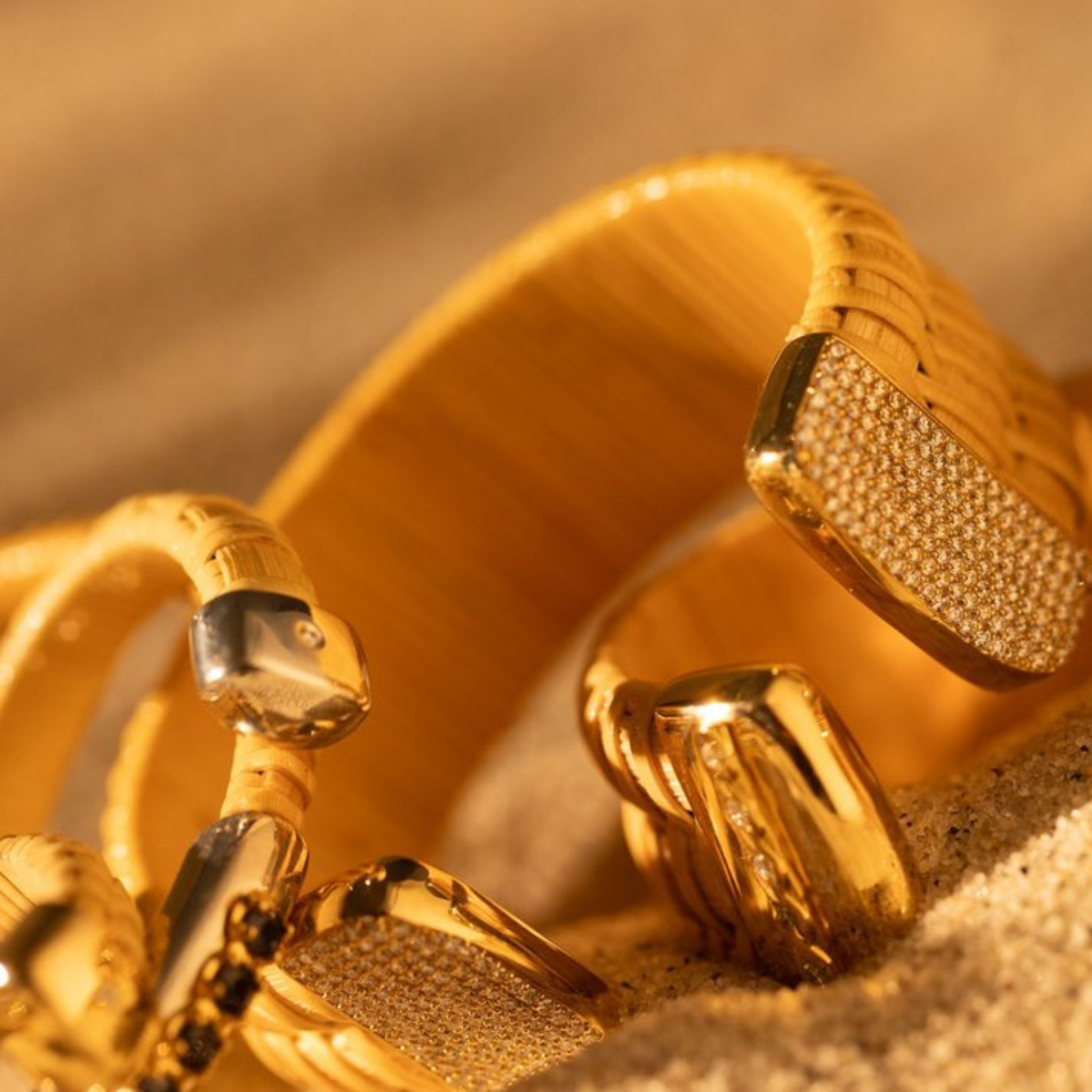 wide woven and narrow woven cuff bracelets with gold and silver caps and diamond accents laying in sand