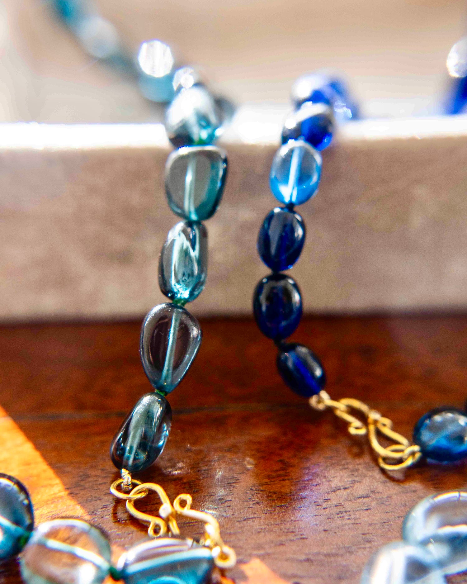 Close-up of two blue beaded necklaces with gold accents on a wooden surface.