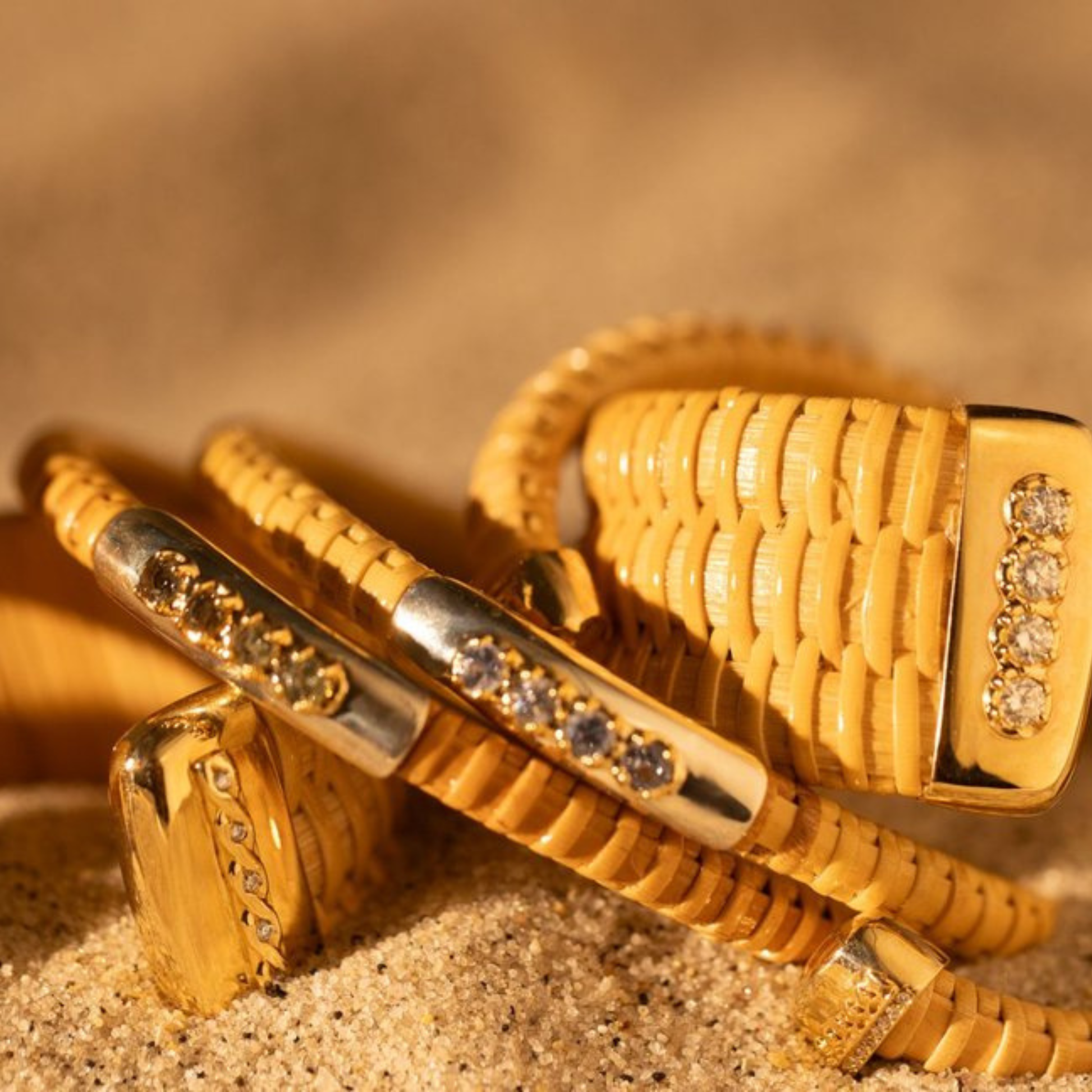 bunch of woven cuff bracelets with gold and silver and gems and diamonds in sand