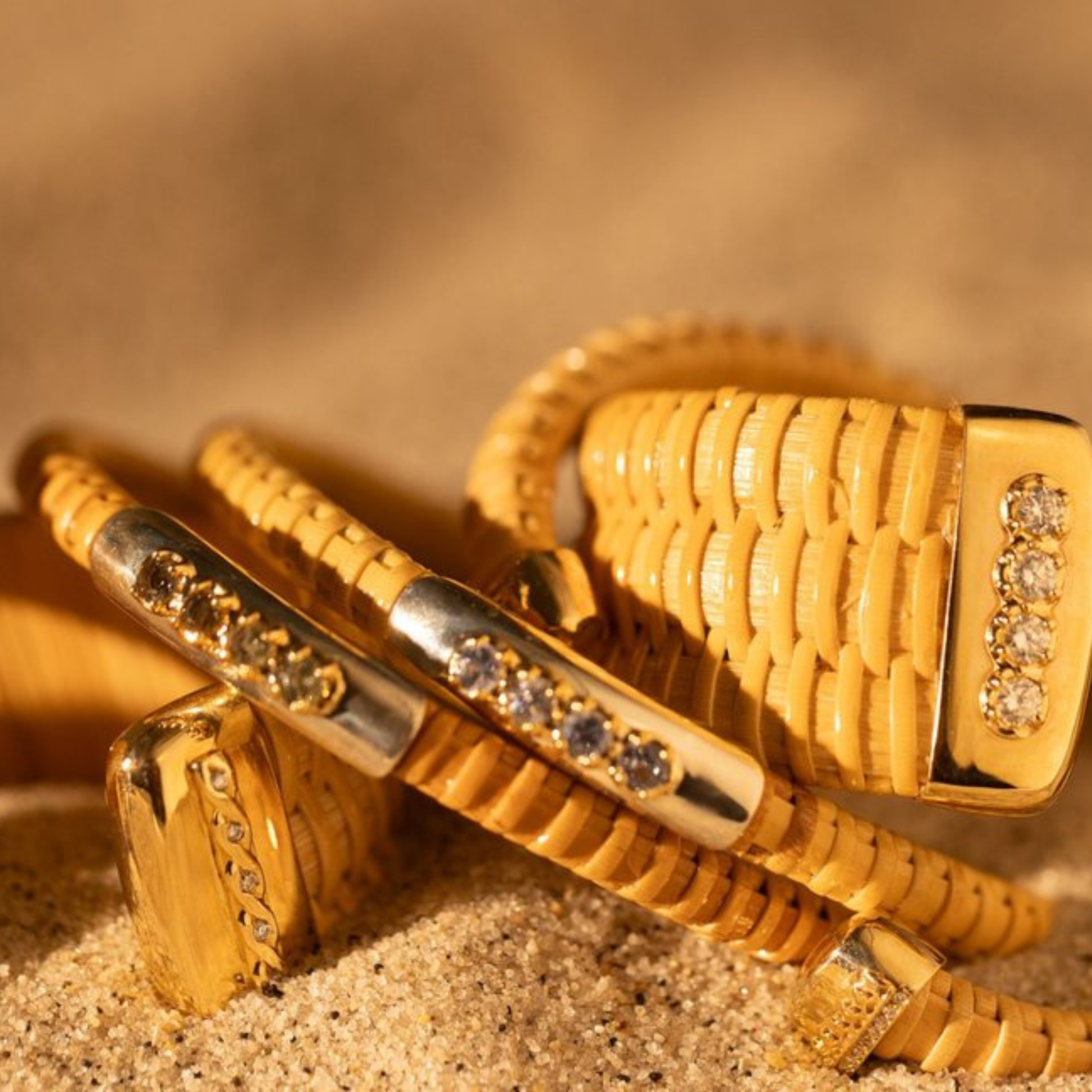 Woven bracelets with diamond and gem accents on a textured regal sandy background