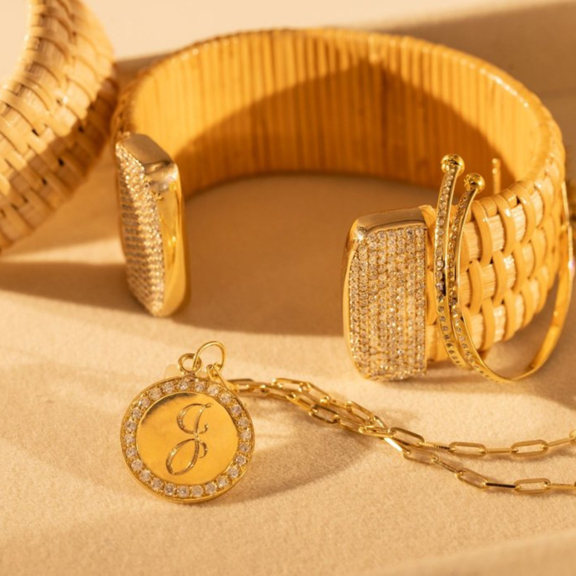 Wide woven cuff bracelet and gold necklace with a pendant and letter "J" inscribed and gold hoop and diamond earrings