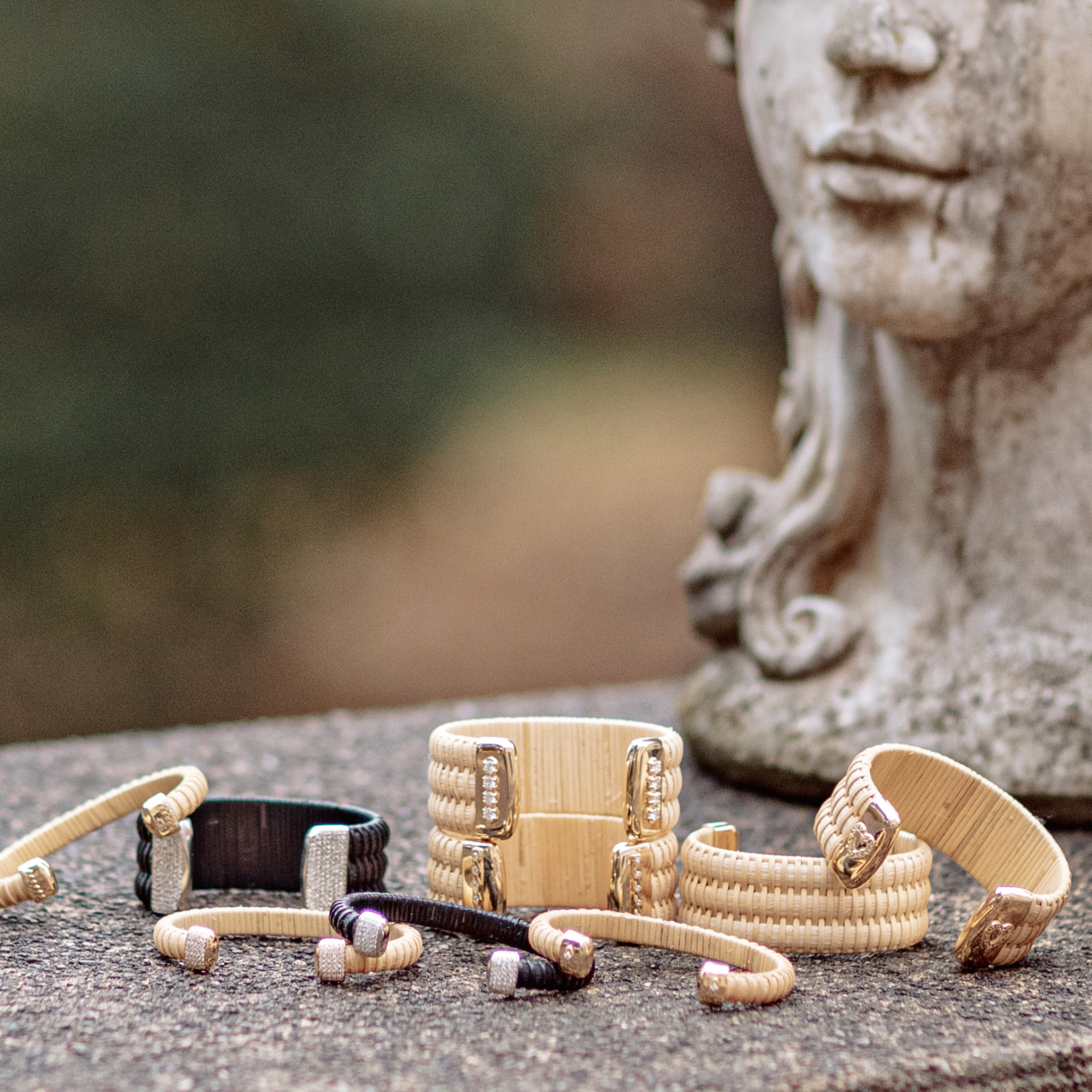Collection of basket weave cuff bracelets on a stone surface with a blurred statue in the background
