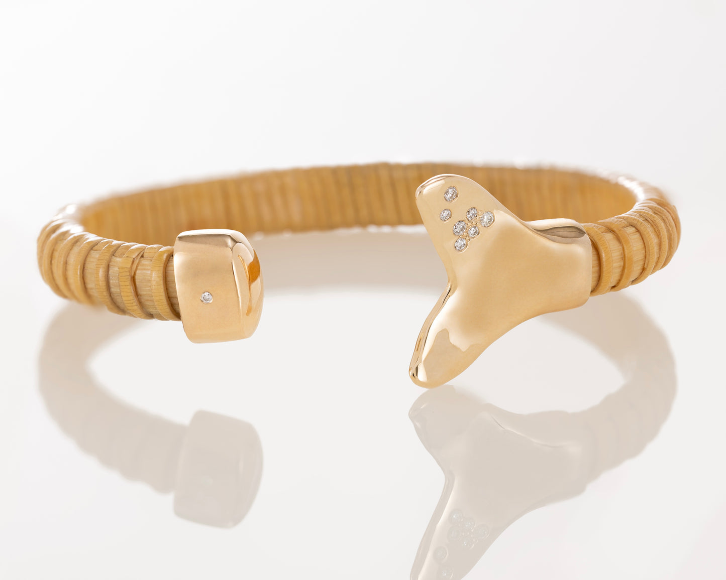 Nantucket Basket bracelet laying on side with gold caps; one shaped as whale tail and one as regular cap, both with diamonds. 