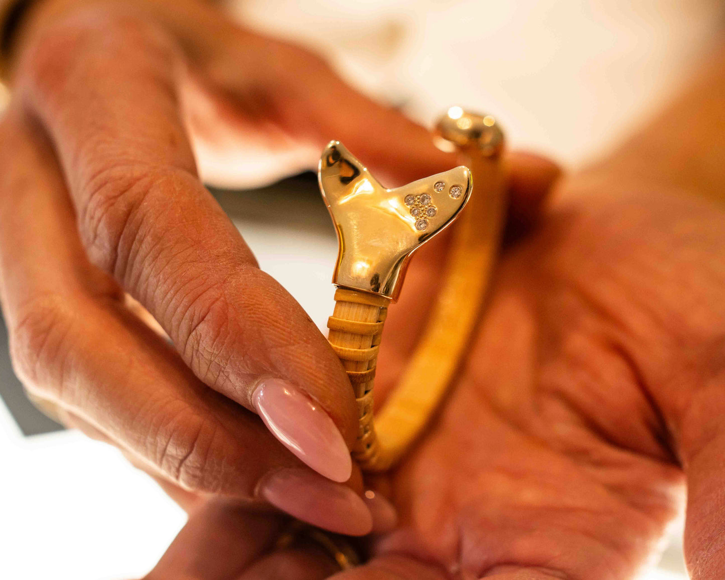 Woman's hand holding Nantucket Basket bracelet with gold caps; focus is on whale tail gold and diamond cap.