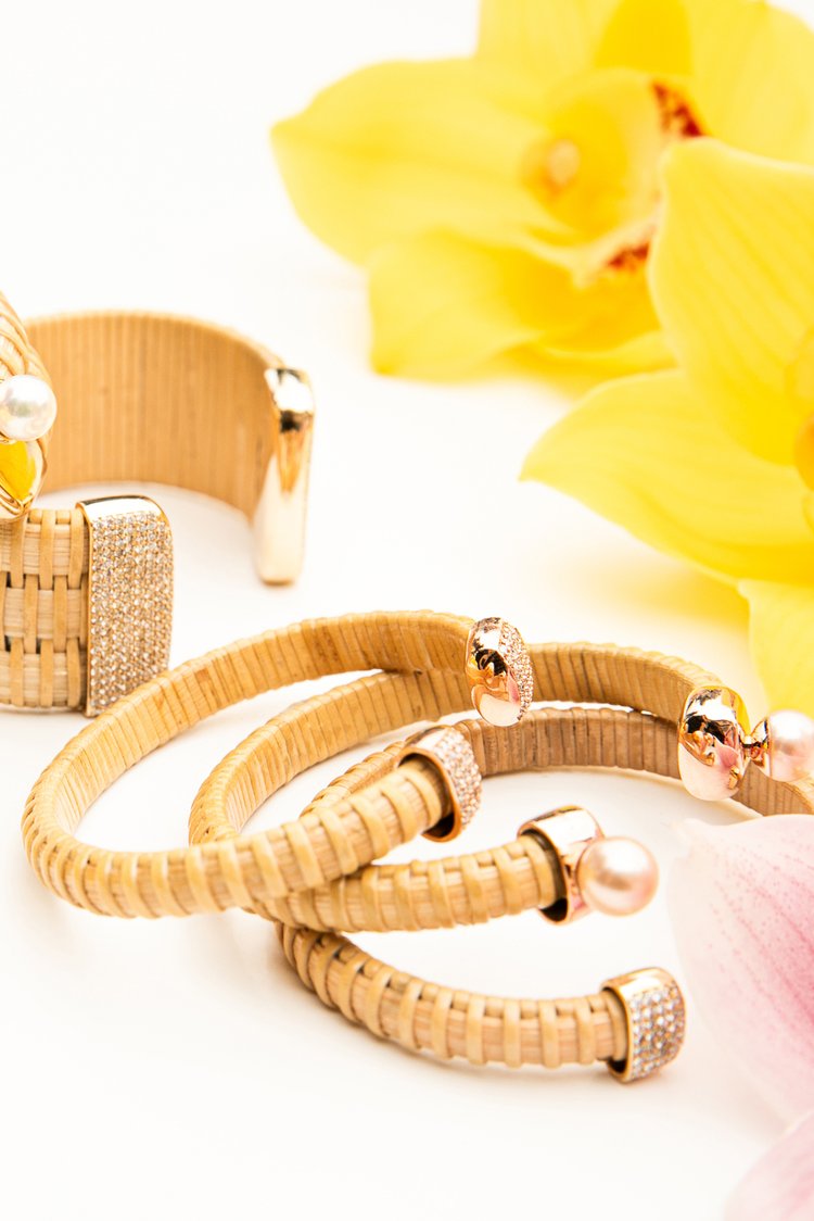 Stack of Hyannis Port Nantucket 1/4" Cuffs, handwoven from natural cane and rattan, with yellow gold diamonds on table with yellow flower in background