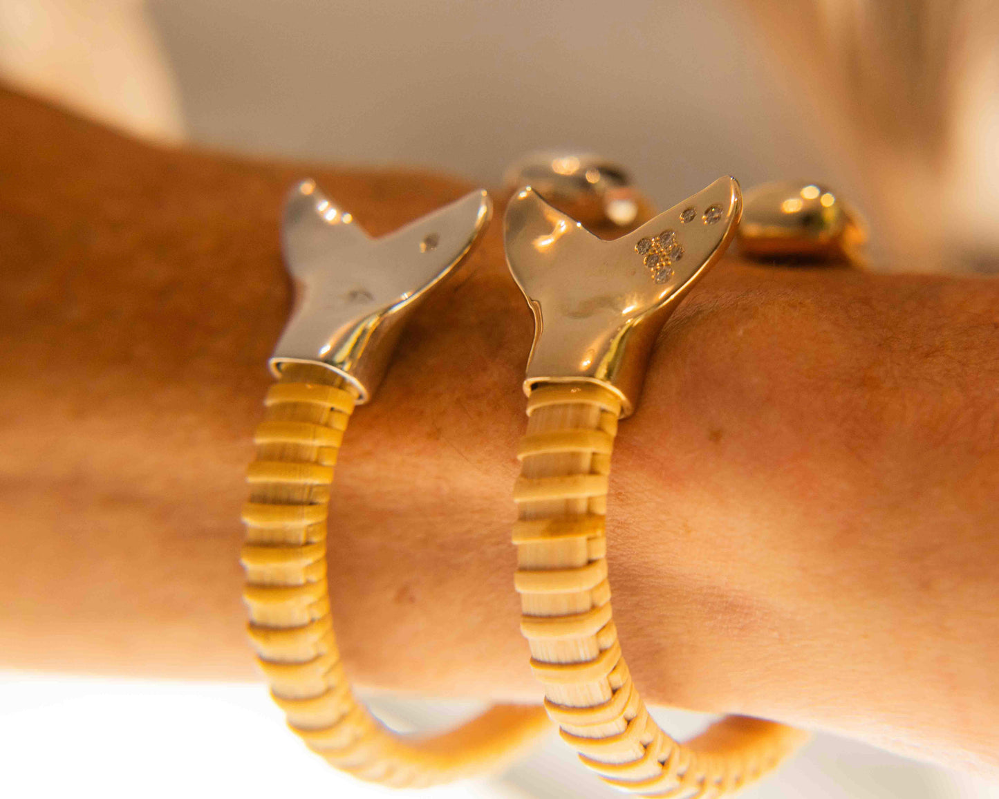 Woman wearing on wrist two Nantucket Basket Cuff Bracelets with silver and gold whale tail caps and diamond accents on plain background