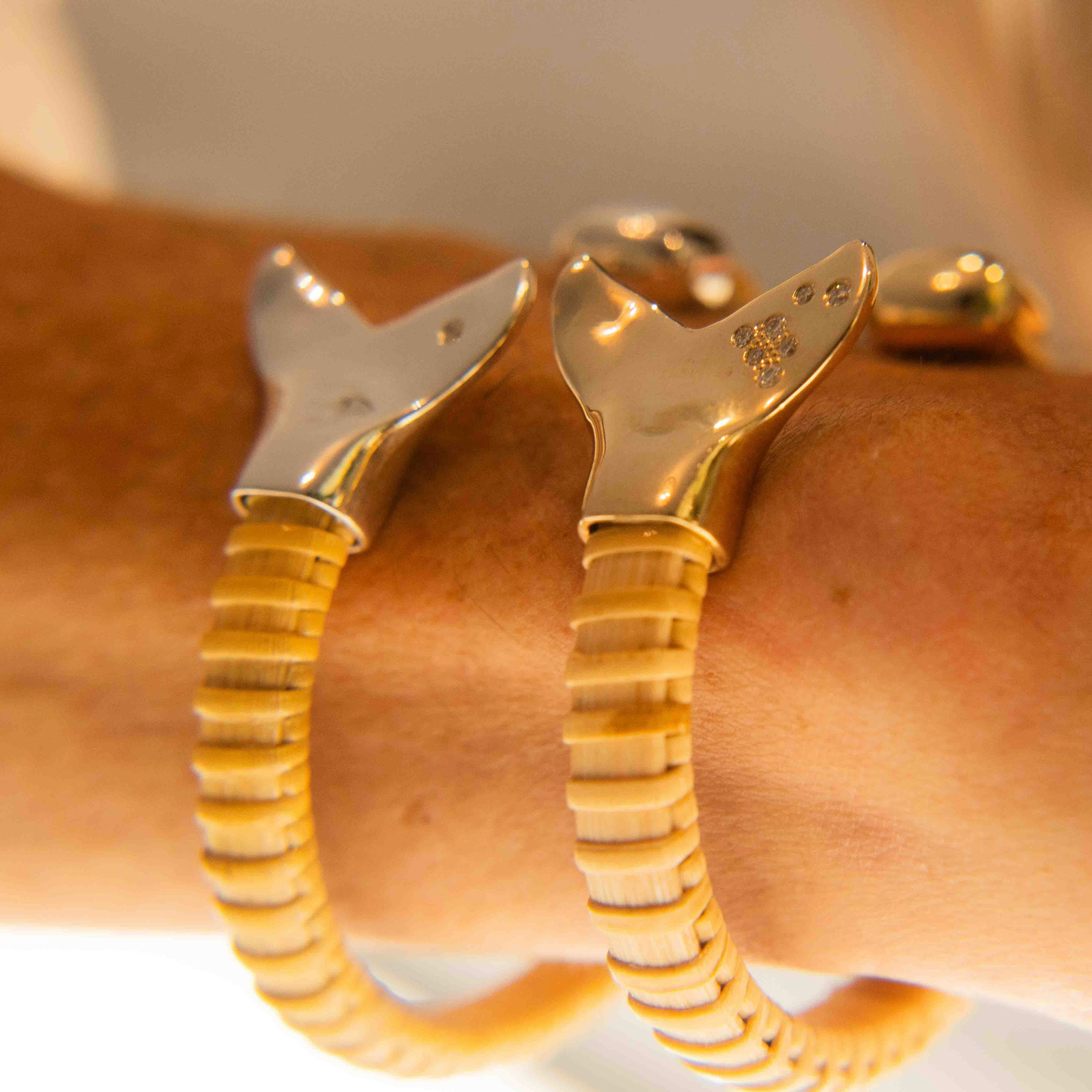 Woman wearing on wrist two Nantucket Basket Cuff Bracelets with silver and gold whale tail caps and diamond accents on plain background