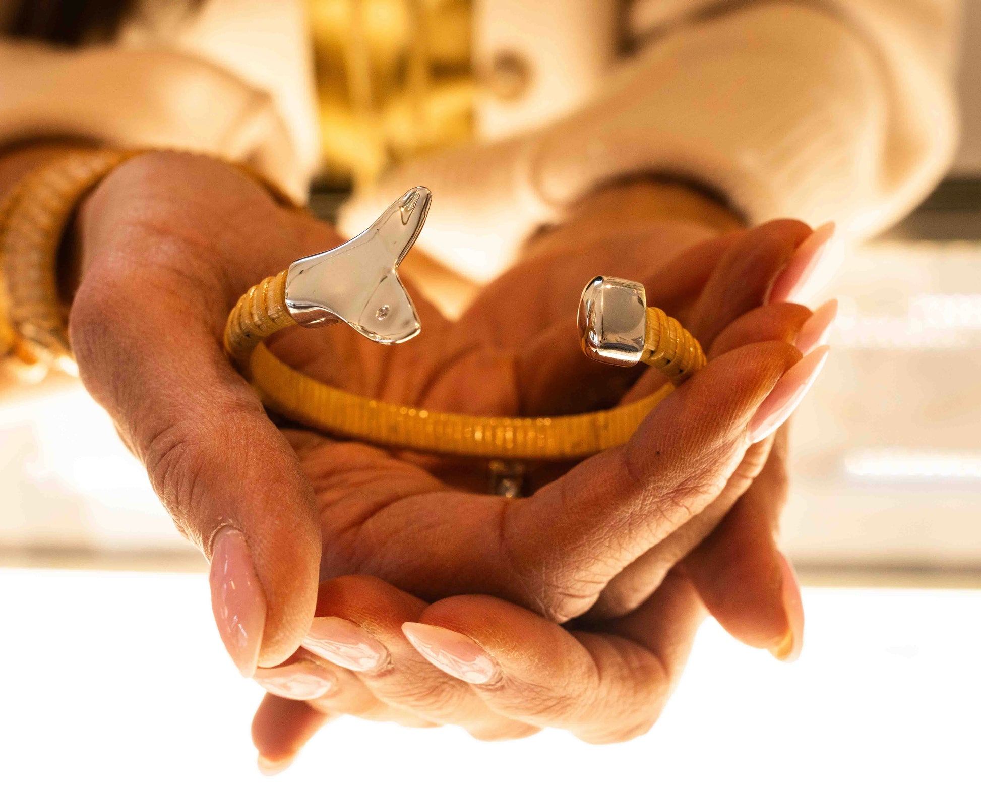 Woman holding Nantucket Basket Cuff Bracelet with silver whale tail caps and diamond accents on plain background
