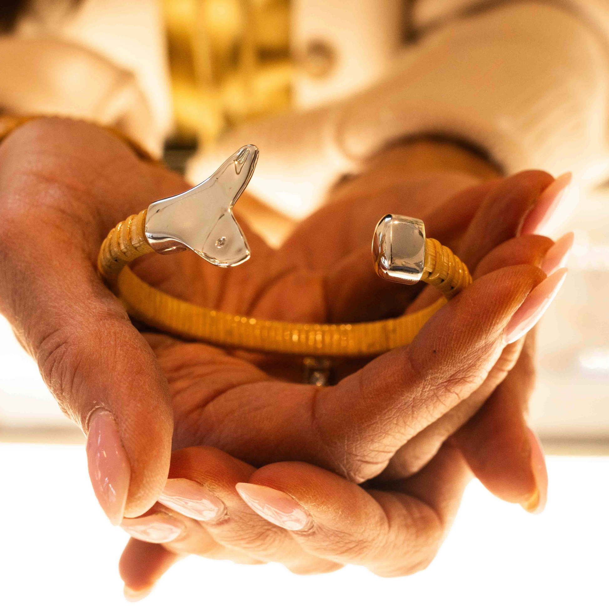 Woman holding Nantucket Basket Cuff Bracelet with silver whale tail caps and diamond accents on plain background