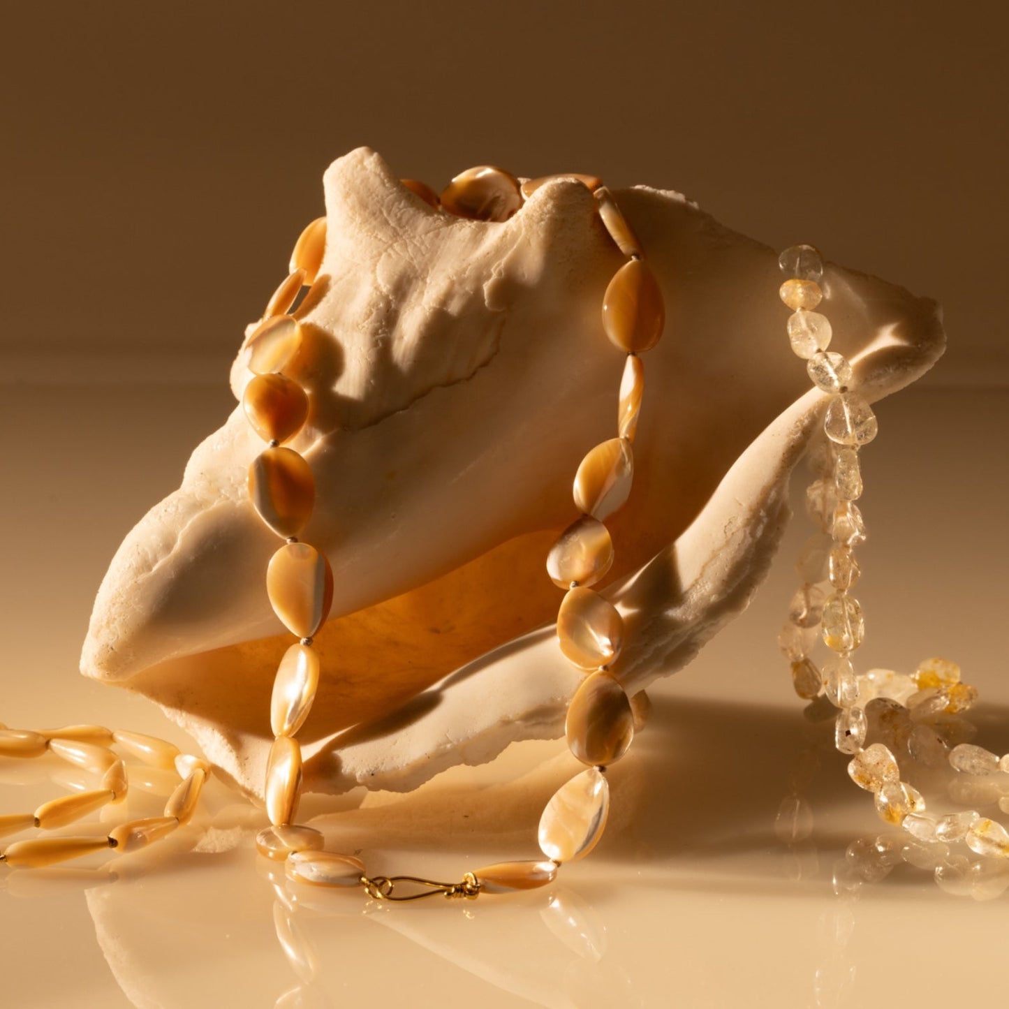 Mother of pearl beaded teardrop necklace draped over a shell