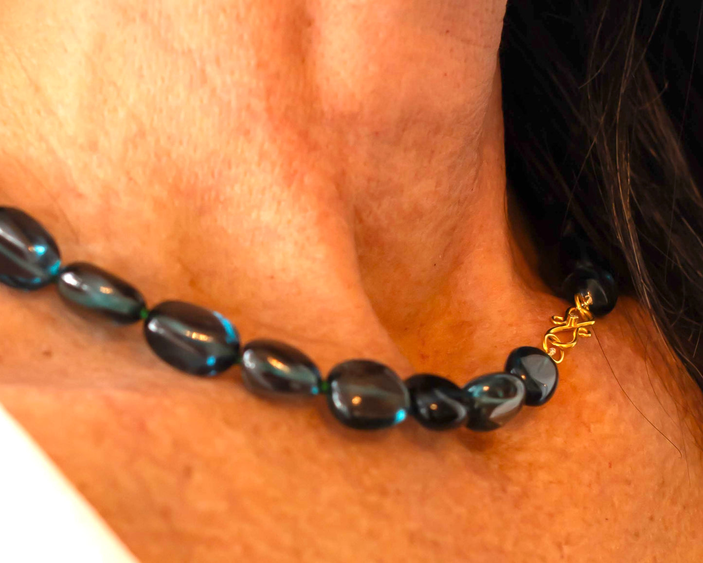 Close up of woman wearing blue beaded necklace with gold clasp around her neck