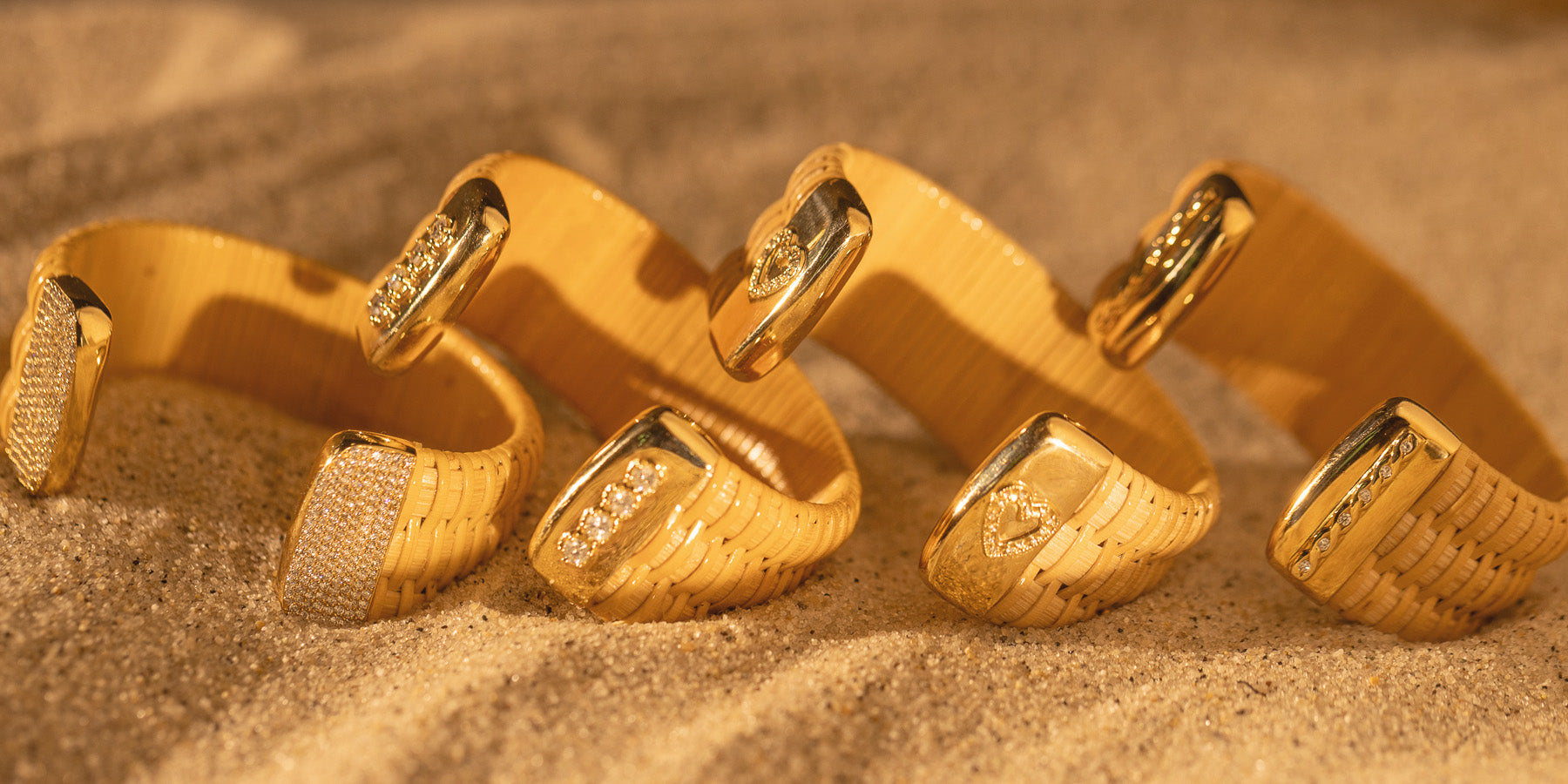 Four Nantucket Lightship Basket Cuff Bracelets capped in gold and diamonds laid in the sand.